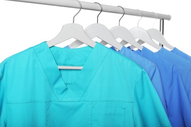 Photo of Turquoise and light blue medical uniforms on rack against white background