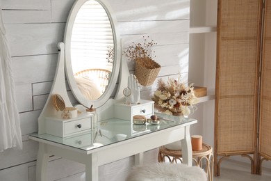 Photo of Wooden dressing table with decorative elements and makeup products in room. Interior design