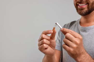 Photo of Stop smoking concept. Man breaking cigarette on grey background, closeup. Space for text