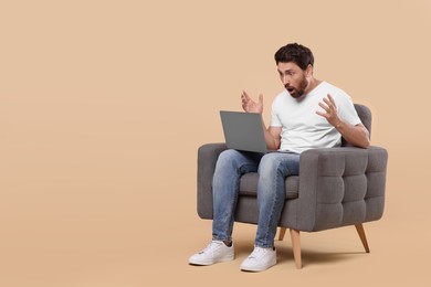 Photo of Emotional man with laptop sitting in armchair against beige background. Space for text