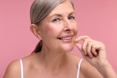 Beautiful woman taking vitamin capsule on pink background