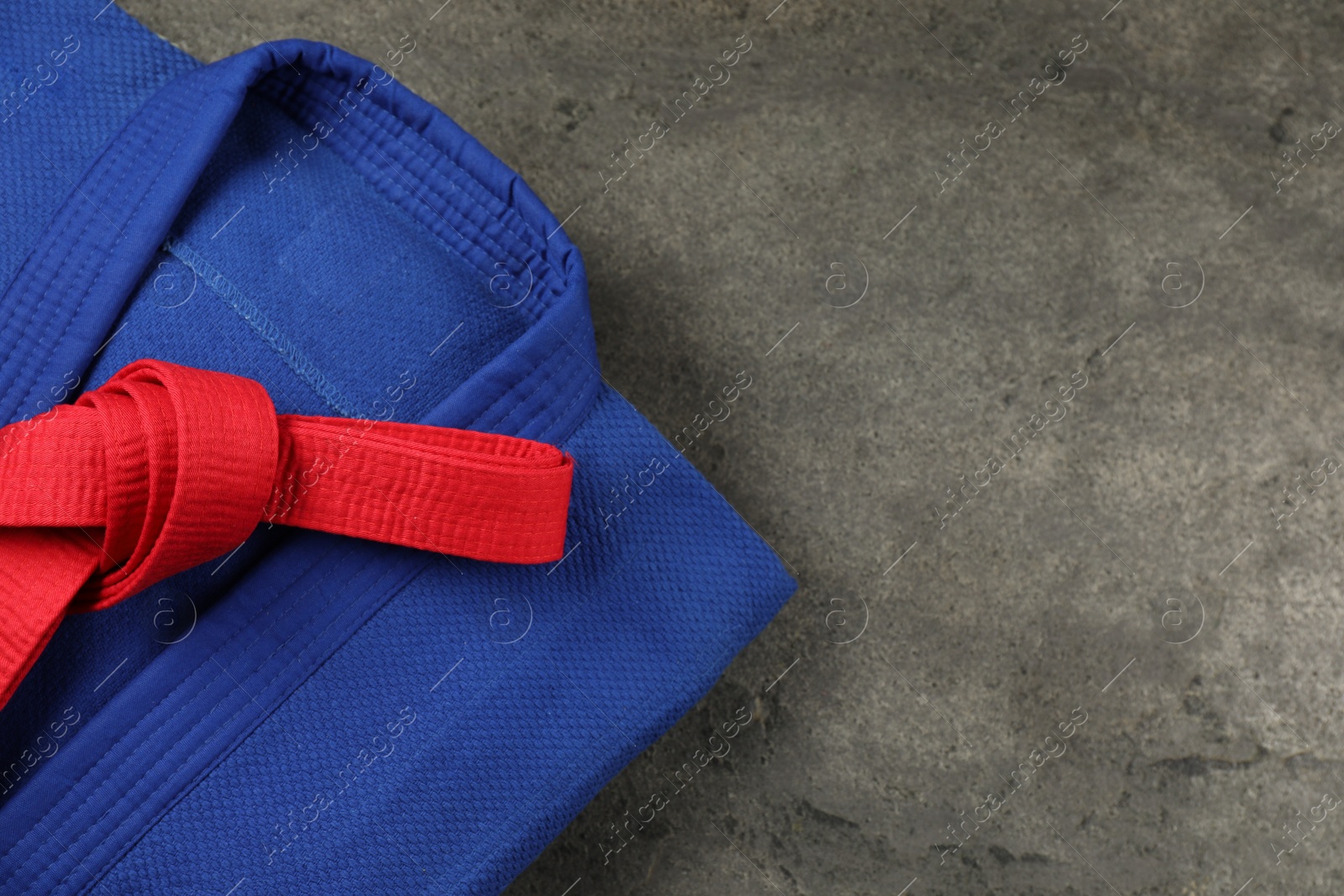 Photo of Red karate belt and blue kimono on gray textured background, top view. Space for text