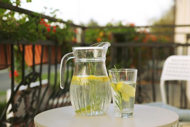 Photo of Jug and glass with refreshing lemon water on light table outdoors