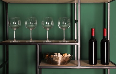 Photo of Bottles of wine, corks and glasses on rack near green wall