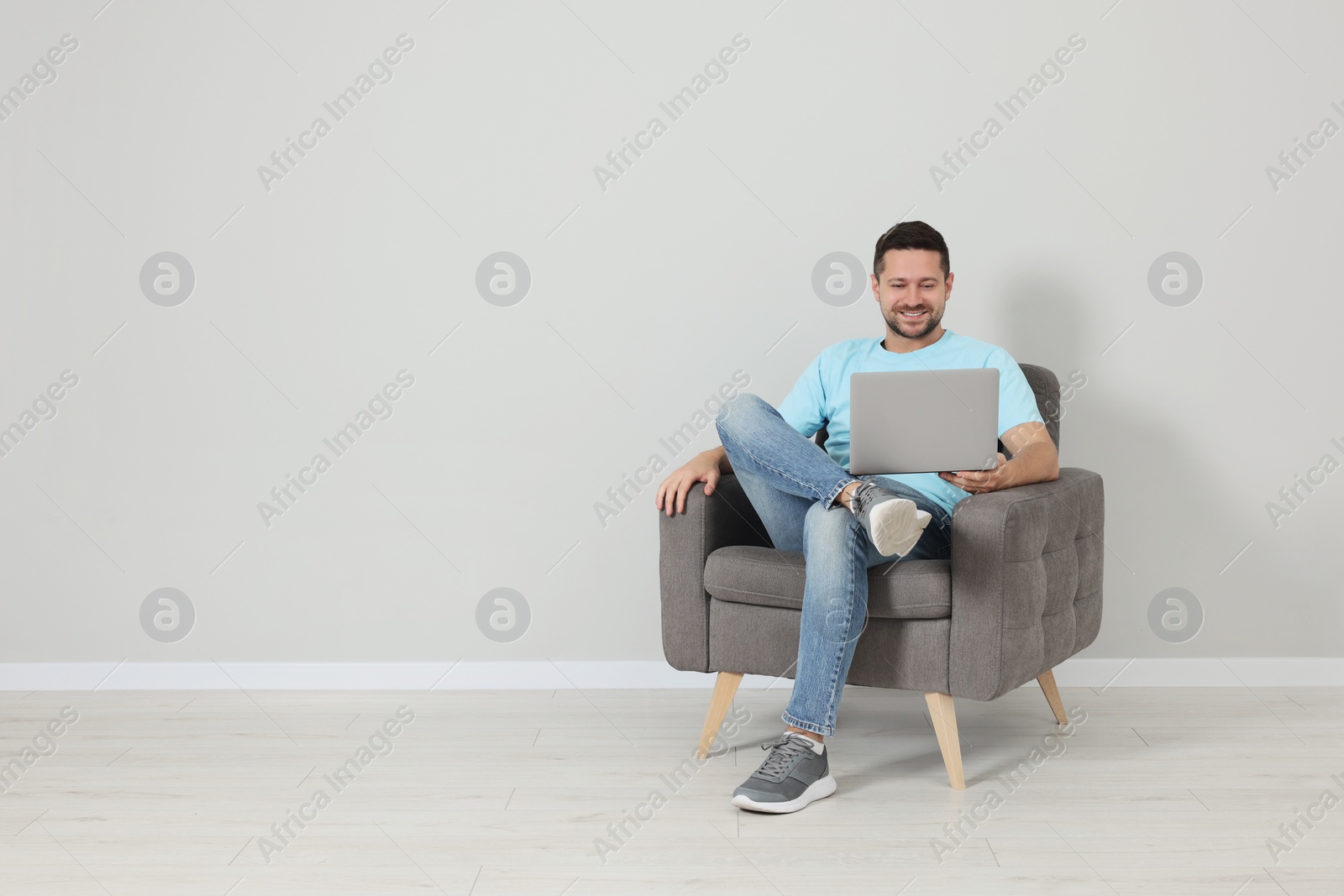 Photo of Happy man sitting in armchair and using laptop indoors, space for text