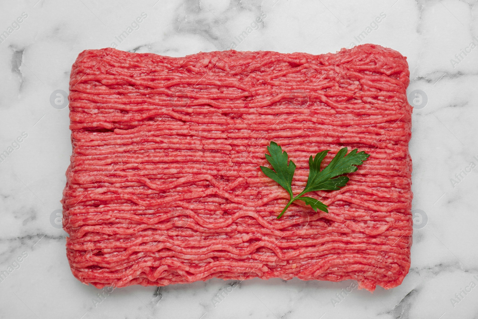 Photo of Raw fresh minced meat with parsley on white marble table, top view