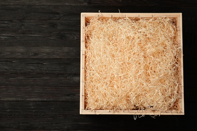 Wooden crate with filler on dark background, top view. Space for text