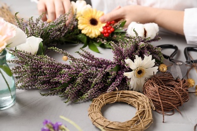 Florist making beautiful autumnal wreath with heather flowers at light grey table, closeup