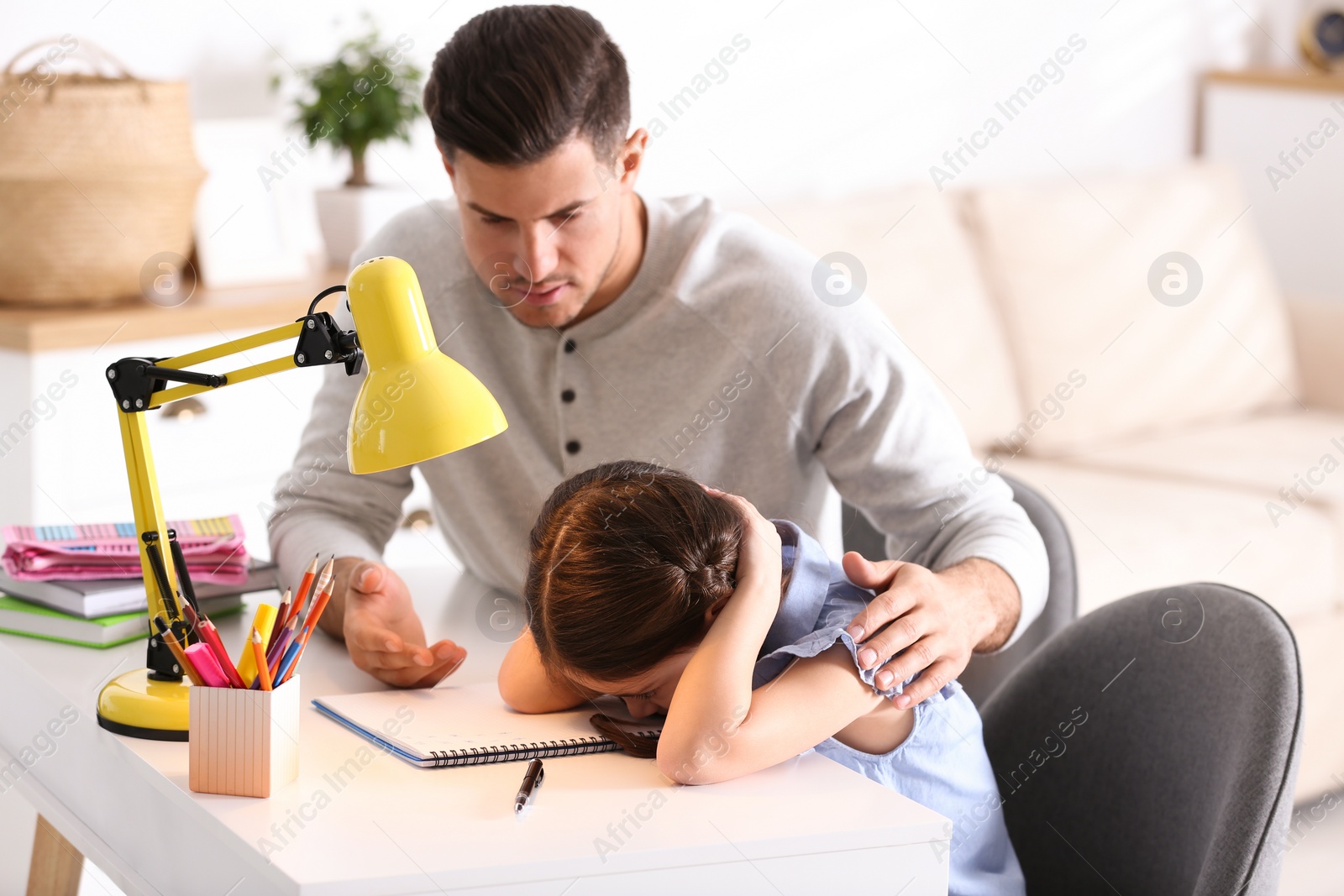 Photo of Father scolding his daughter while helping with homework at table indoors