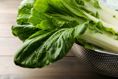 Photo of Fresh green pak choy cabbages with water drops in colander on wooden table, closeup