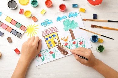 Photo of Girl painting picture of house on table, top view