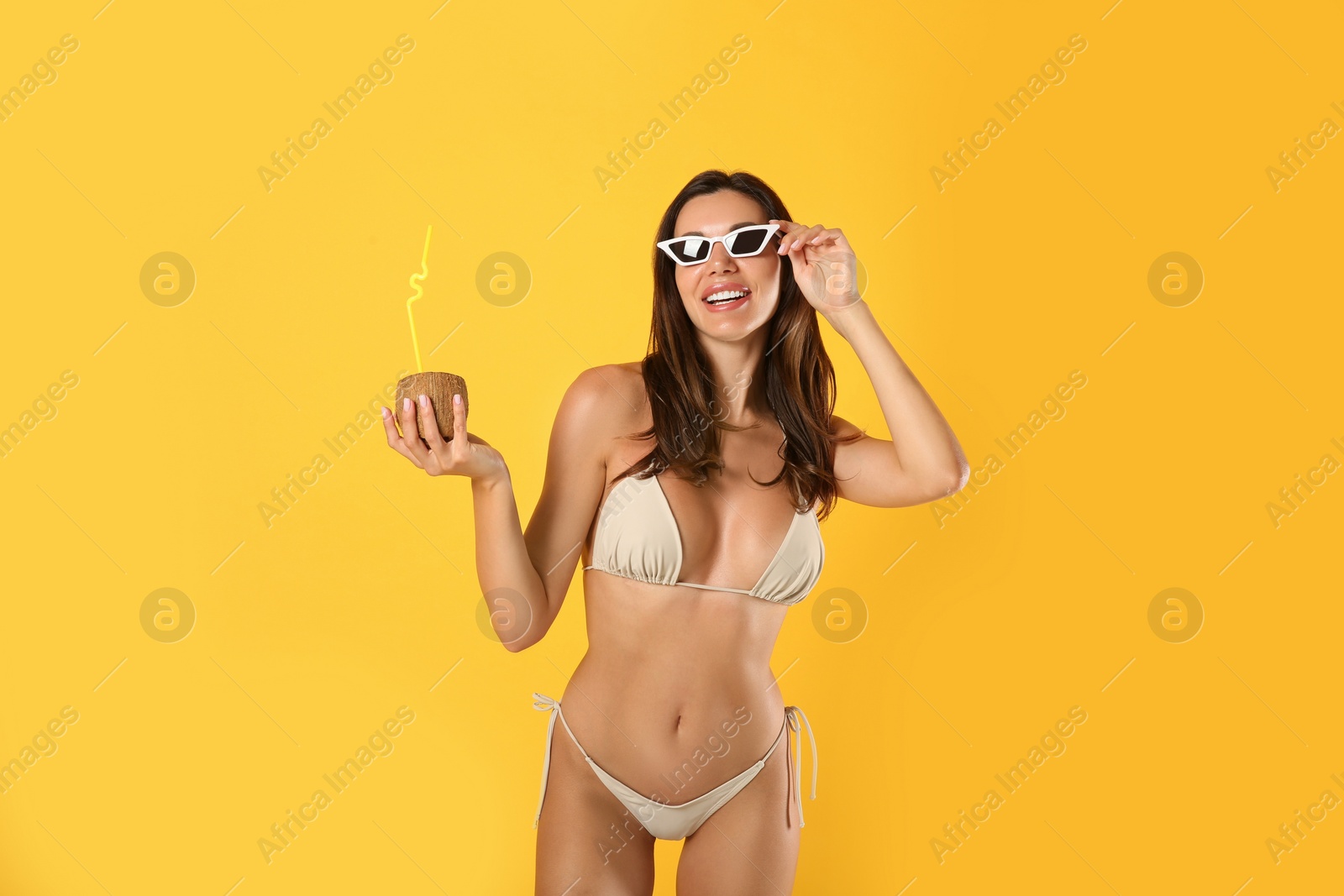 Photo of Beautiful woman in stylish bikini with tropical cocktail on yellow background