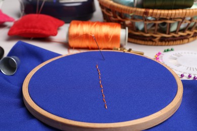 Photo of Blue cloth with stitches, sewing thread and needle on table, closeup