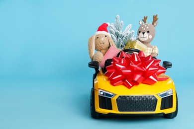 Child's electric car with toys, gift boxes and Christmas decor on light blue background, space for text