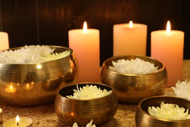 Tibetan singing bowls with beautiful flowers and burning candles on table