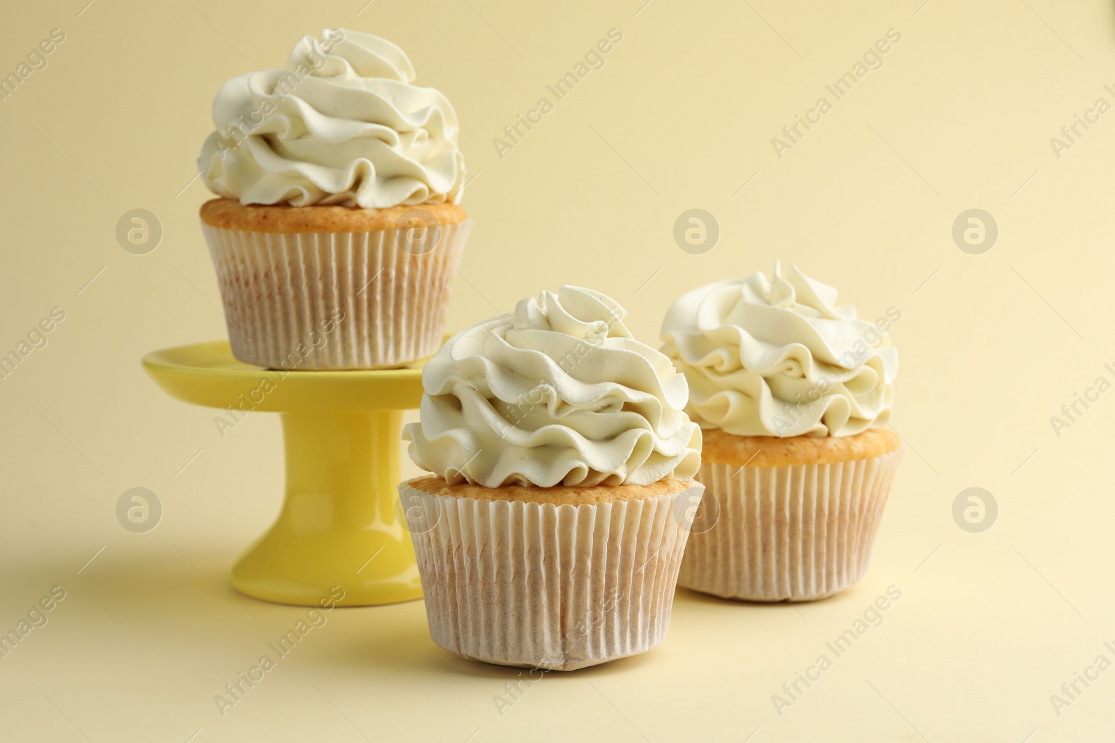 Photo of Tasty vanilla cupcakes with cream on pale yellow background