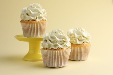 Tasty vanilla cupcakes with cream on pale yellow background