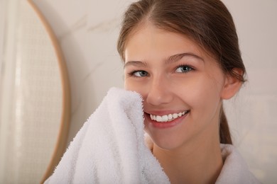 Photo of Beautiful teenage girl wiping face with towel at home, closeup