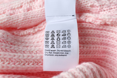 Photo of Clothing label with care symbols on pink sweater, closeup view