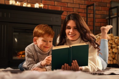 Happy mother and son reading together on floor near fireplace at home