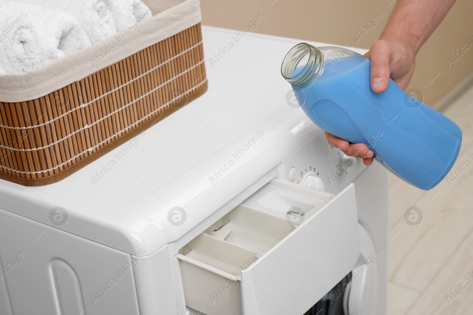 Photo of Man pouring fabric softener from bottle into washing machine indoors, closeup