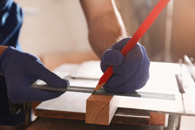 Photo of Professional carpenter making mark on wooden bar in workshop, closeup