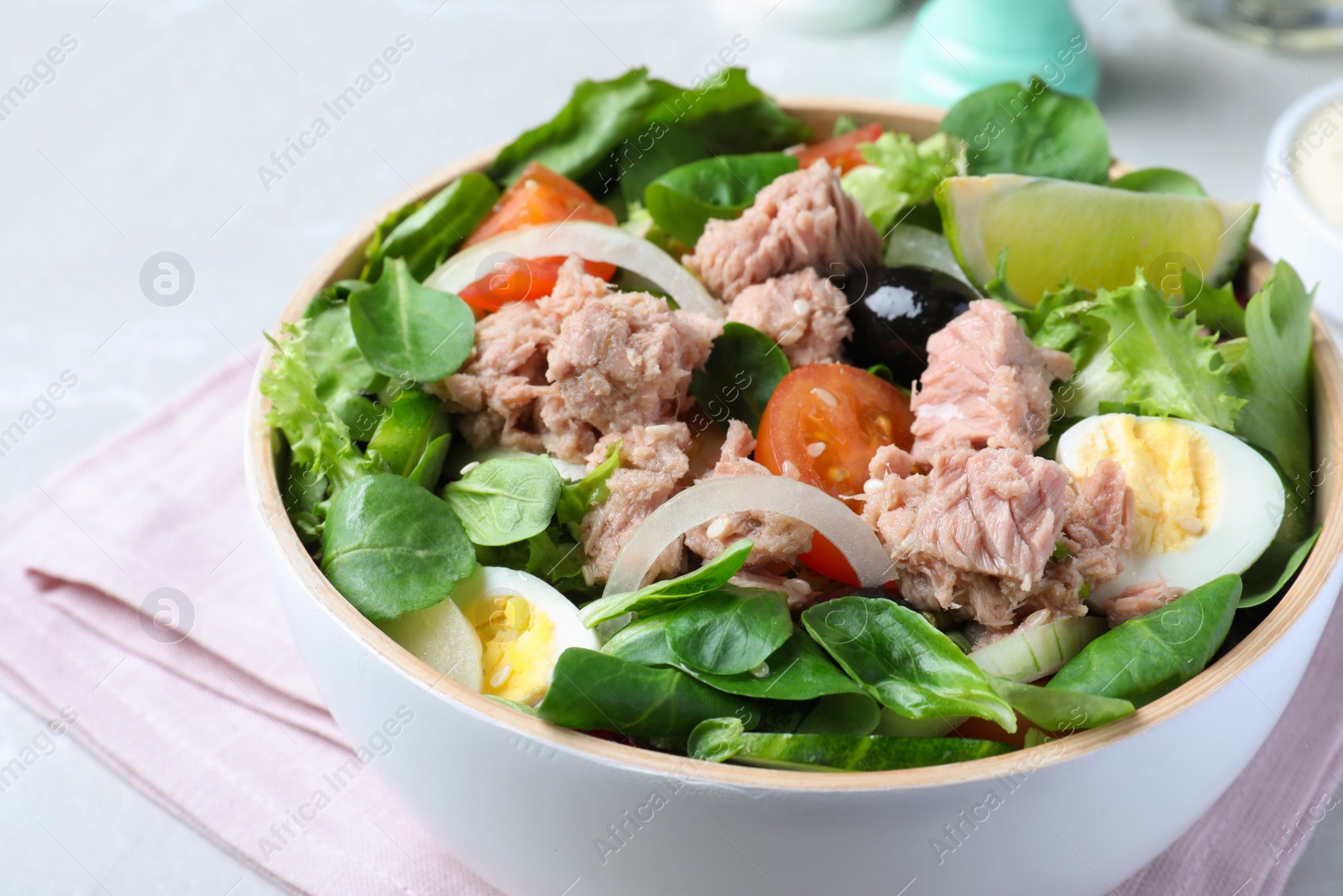 Photo of Bowl of delicious salad with canned tuna and vegetables on light table, closeup