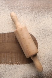 Photo of Imprint of board on wooden table with flour and rolling pin, top view