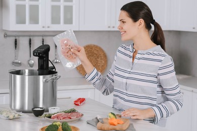 Photo of Woman putting vacuum packed meat into pot with sous vide cooker in kitchen. Thermal immersion circulator