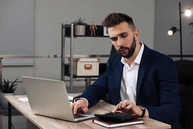 Man with calculator working on laptop at table in office, space for text