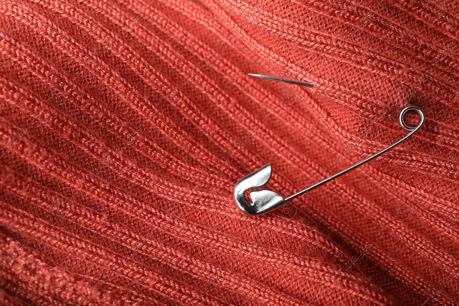 Photo of Metal safety pin on coral fabric, closeup