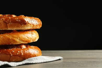 Tasty freshly baked pretzels on wooden table against black background. Space for text