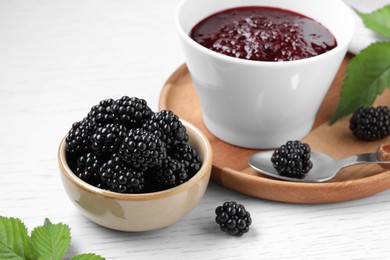 Photo of Fresh ripe blackberries, tasty jam and leaves on white wooden table, closeup