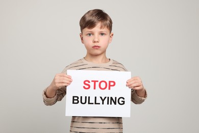 Photo of Boy holding sign with phrase Stop Bullying on light grey background