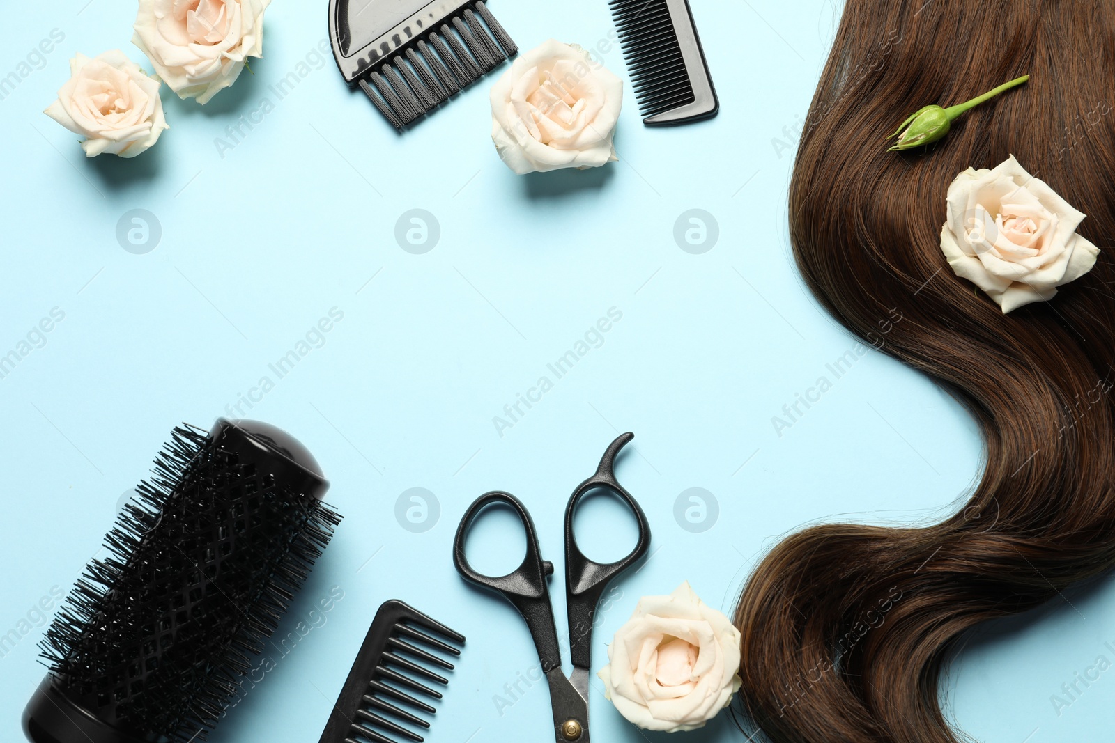 Photo of Flat lay composition with professional hairdresser tools, flowers and brown hair strand on light blue background. Space for text