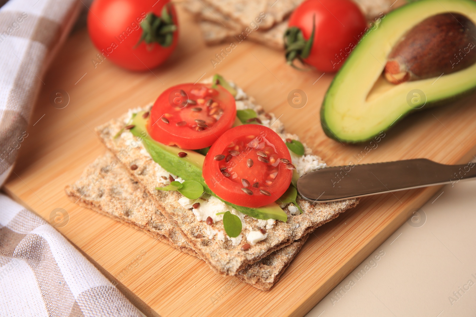 Photo of Fresh crunchy crispbreads with cream cheese, tomatoes and avocado on beige table, closeup