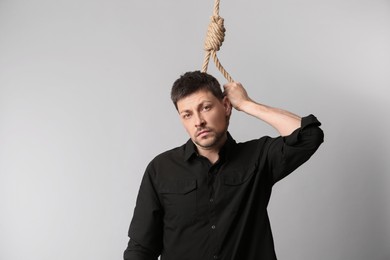 Photo of Depressed man with rope noose on neck against light background