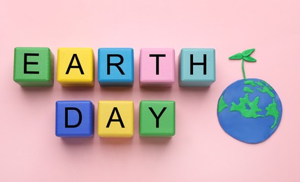 Photo of Phrase Earth Day made with cubes and model of planet on pink background, flat lay