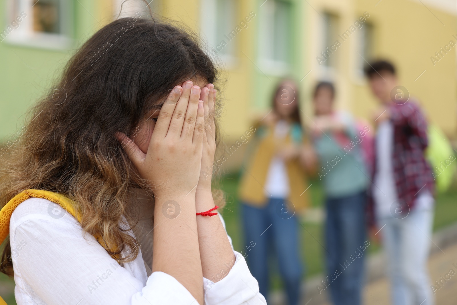 Photo of Teen problems. Group of students pointing at upset girl outdoors, selective focus