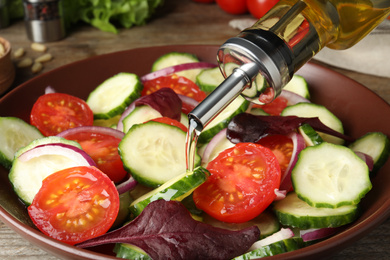 Photo of Adding cooking oil to delicious salad on table, closeup