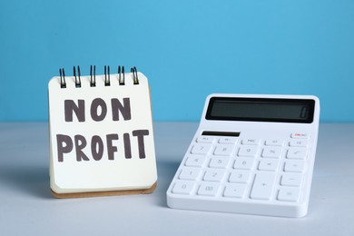 Photo of Notebook with phrase Non Profit and calculator on white table