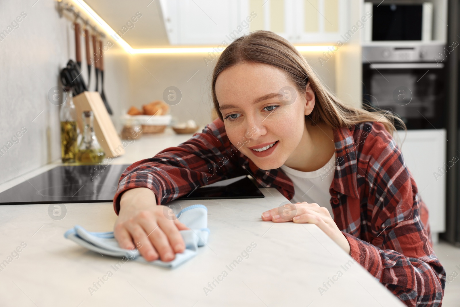 Photo of Woman with microfiber cloth cleaning white marble countertop in kitchen