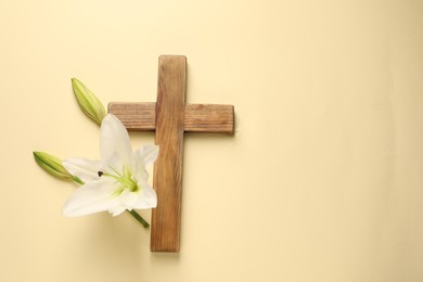 Photo of Wooden cross and lily flowers on pale yellow background, top view with space for text. Easter attributes