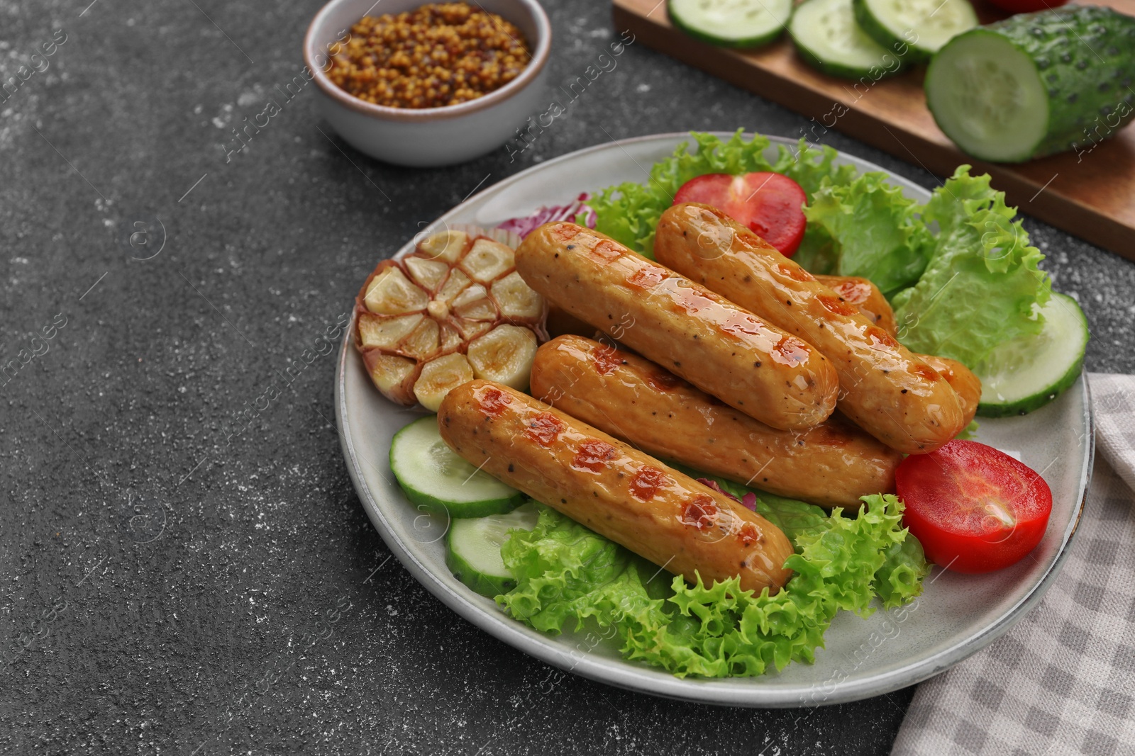 Photo of Delicious grilled vegan sausages with fresh herbs and vegetables on grey table, space for text