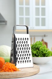 Grater and fresh ripe carrot on white table in kitchen
