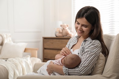 Young woman breastfeeding her little baby at home, space for text