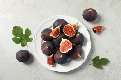 Photo of Whole and cut ripe figs with leaves on light textured table, flat lay