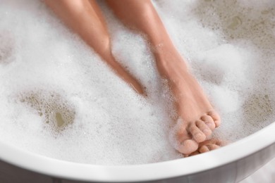 Woman taking bath in tub with foam, closeup