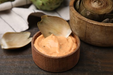 Photo of Delicious cooked artichoke with tasty sauce on wooden table, closeup