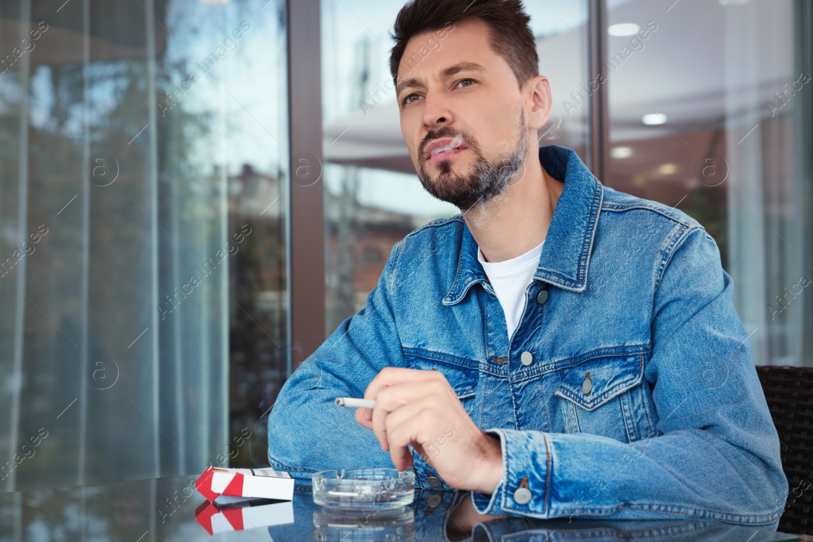 Photo of Handsome man smoking cigarette at table in outdoor cafe